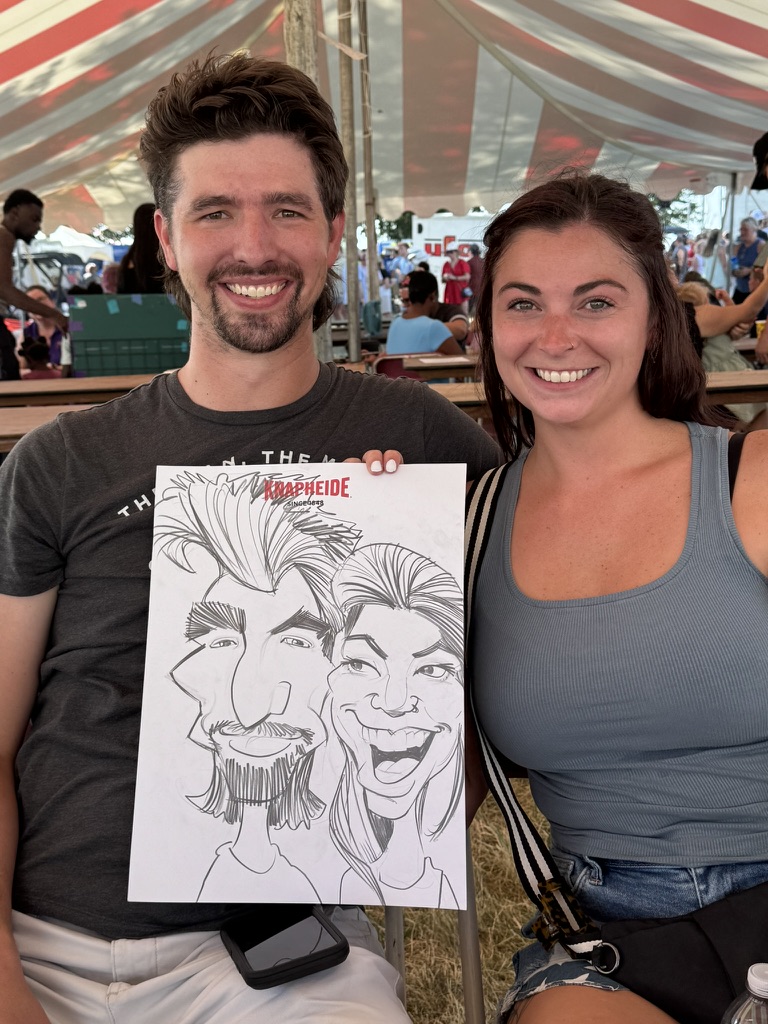 Two guests at an outdoor event hold a playful black-and-white caricature